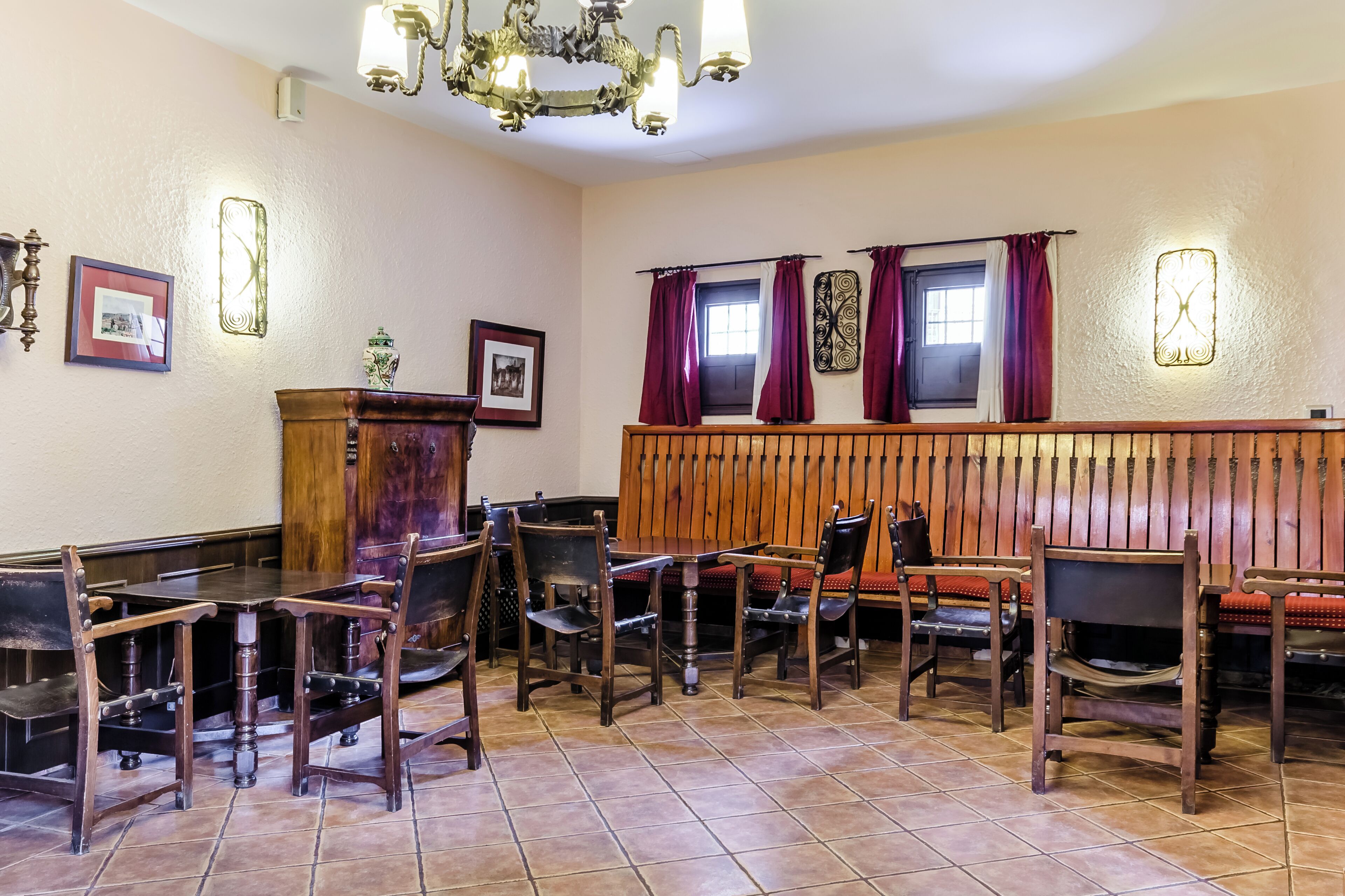 A dining area with wooden tables and chairs, a wooden bench, and a chandelier.