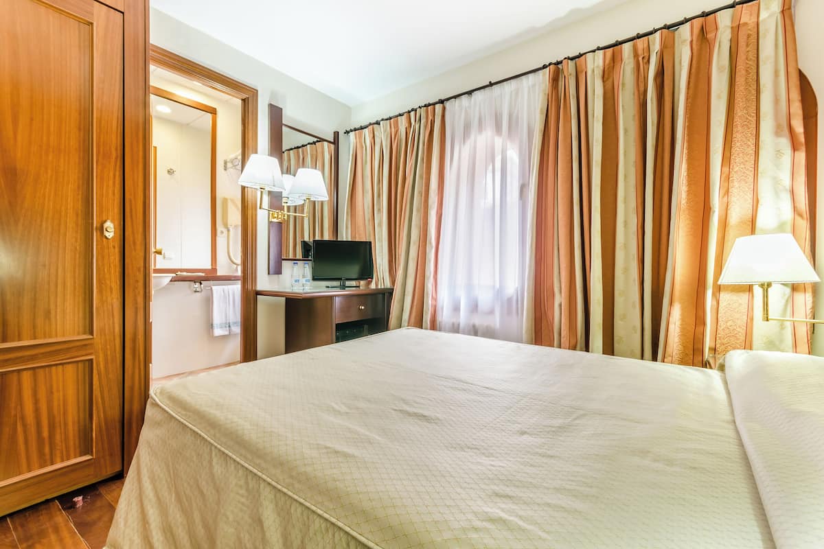 A hotel room with a large bed, a desk with a computer, a TV, and two lamps.