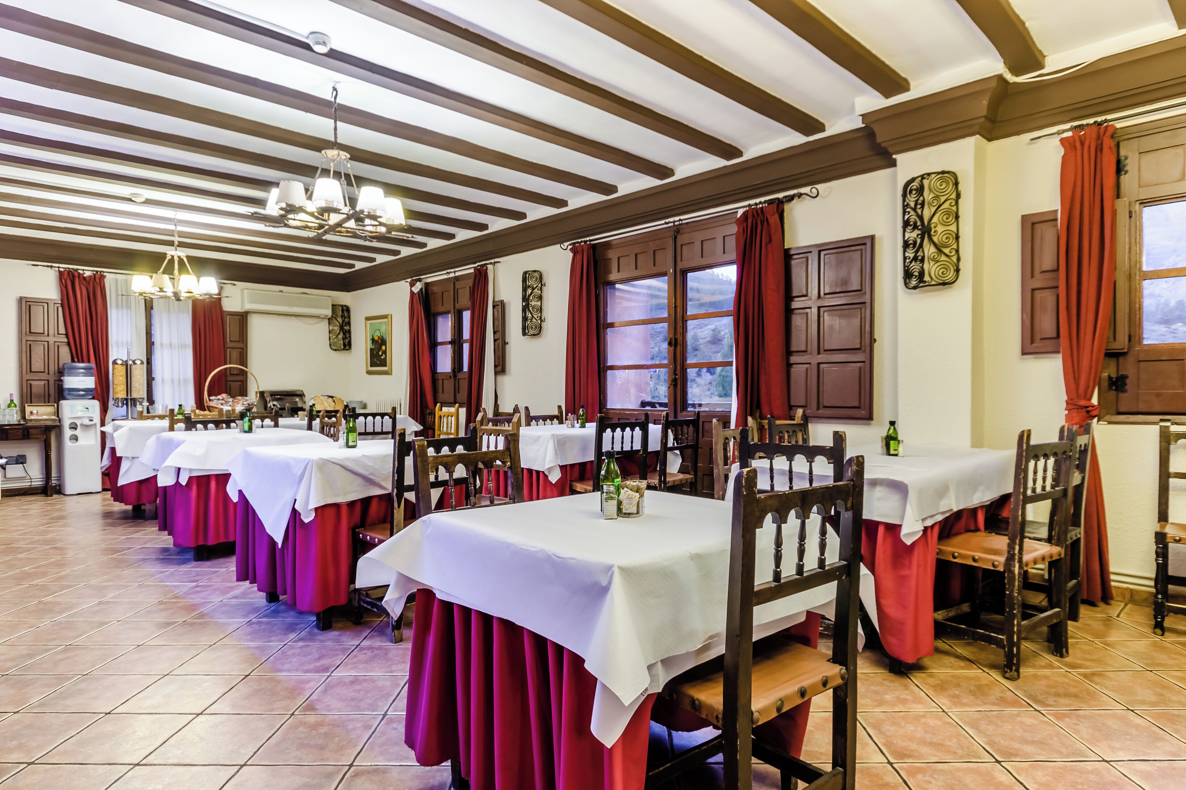 A dining area with multiple tables, red curtains, and wooden chairs.