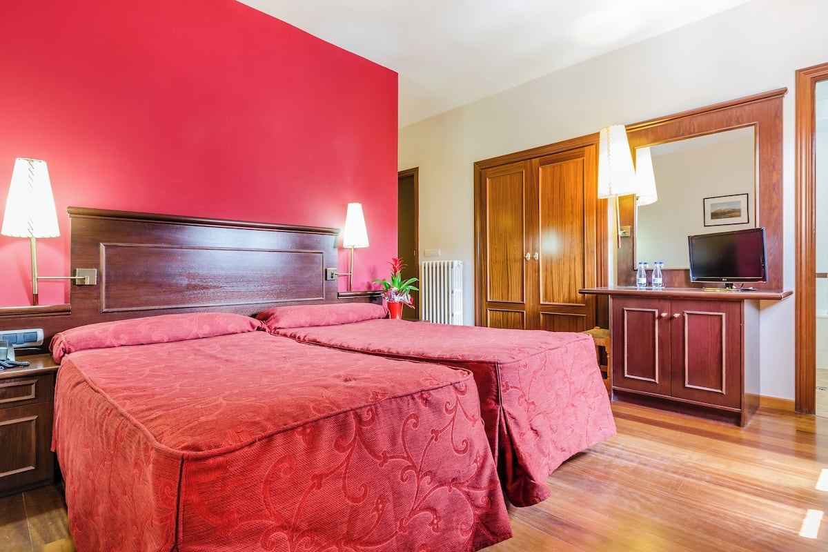 A hotel room with a large bed, a wooden wardrobe, a desk with a lamp, and a television.