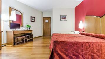 A hotel room with a wooden desk, a bed with a red bedspread, a mirror, and a door.