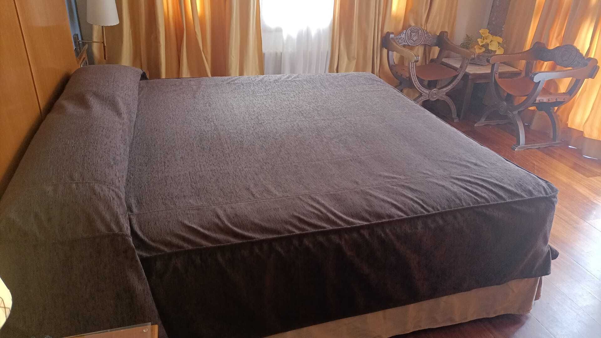 A single bed with a dark mattress in a room with wooden flooring and curtains.