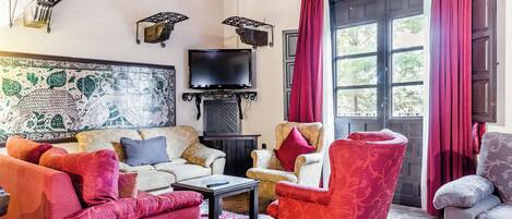 A cozy living room with a sofa, armchairs, a coffee table, and a flat-screen TV mounted on the wall.