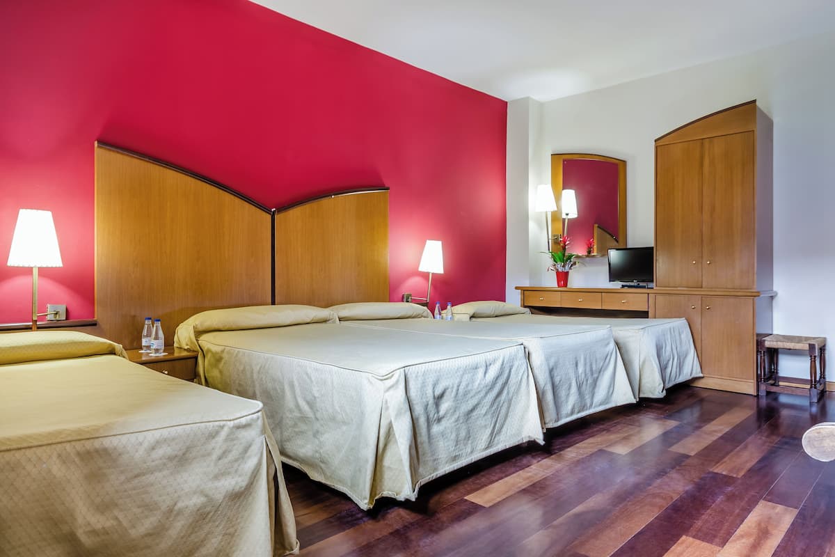 A hotel room with two beds, a TV, a wardrobe, and a desk with a lamp.