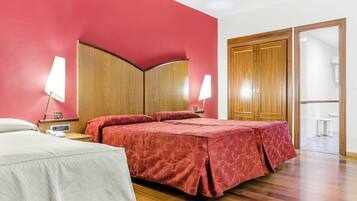 Habitación de hotel con cama, mesitas de noche, lámparas, un armario de madera y un baño visible a través de una puerta abierta.