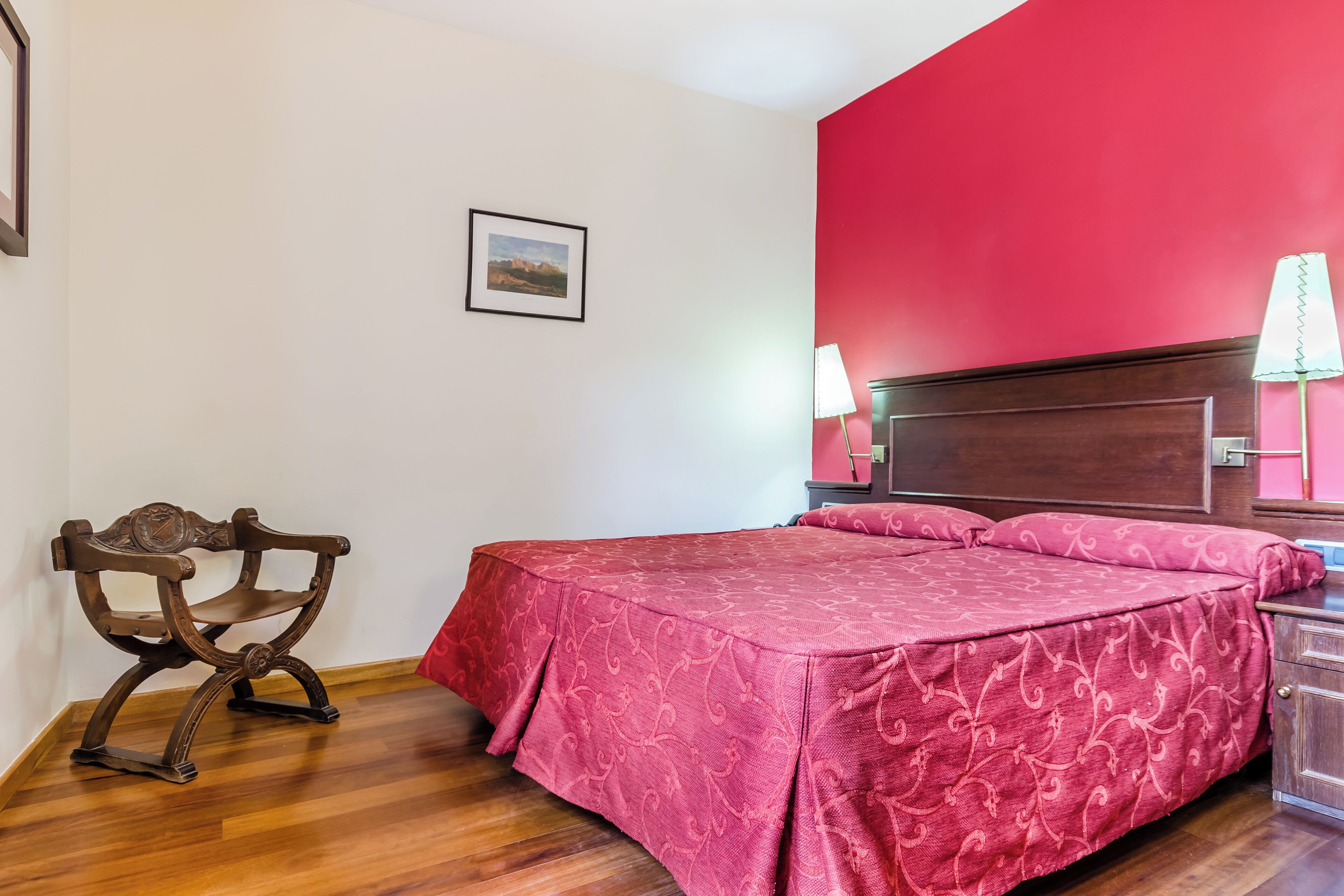 A bedroom with a wooden bed, a red wall, and a wooden bench.