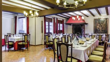 A dining area with multiple tables set for a meal, wooden chairs, and a chandelier.