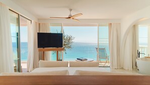 A bedroom with a large bed, a ceiling fan, a TV, and a view of the ocean.
