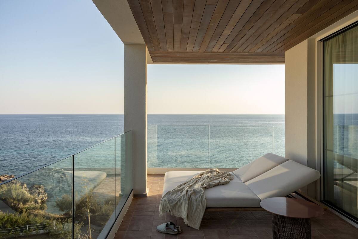 Un balcon avec vue sur la mer, un canapé blanc et une paire de chaussures posées sur le sol.