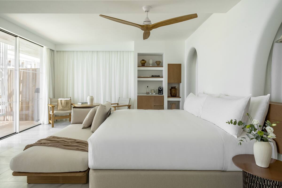 Une chambre d’hôtel moderne dotée d’un grand lit, d’un ventilateur de plafond, d’un bureau et offrant une vue sur l’extérieur.