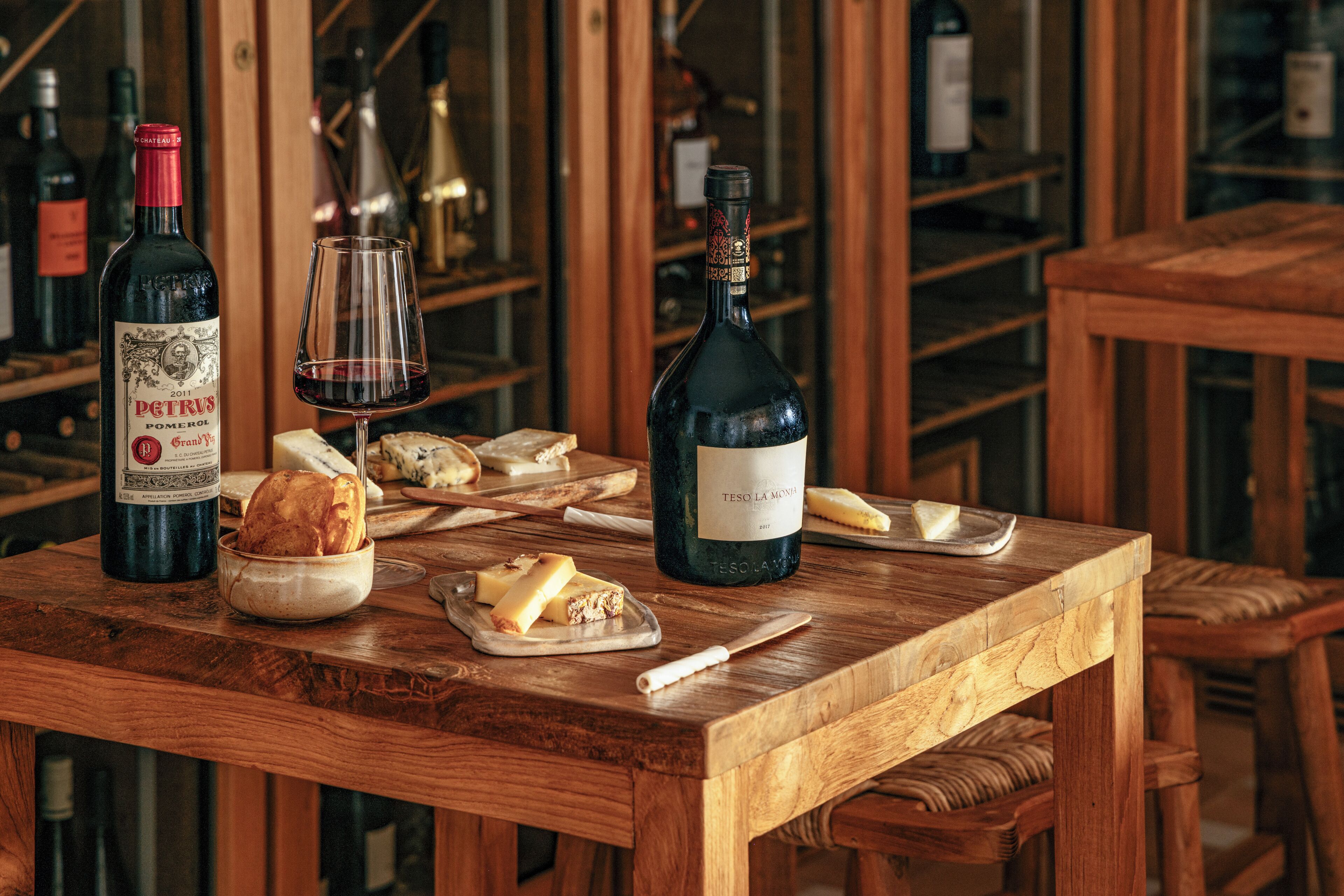 A wooden table with wine bottles, glasses, and cheese.