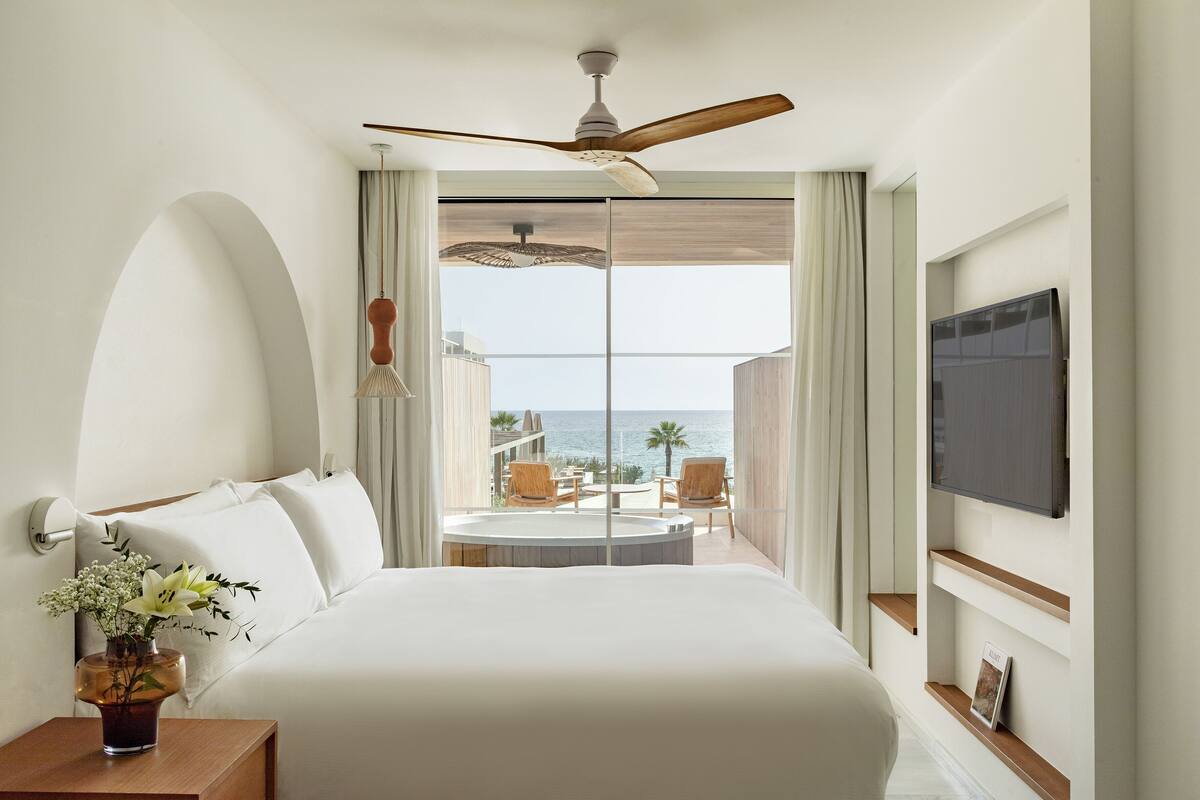 Une chambre d’hôtel avec un grand lit, un ventilateur de plafond, une télévision et un balcon avec vue sur l’océan.