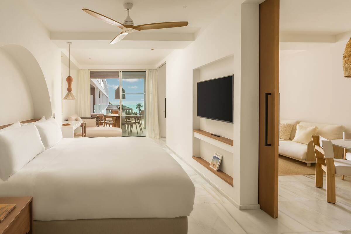 Une chambre d’hôtel moderne dotée d’un grand lit, d’une télévision, d’un balcon avec vue sur l’océan et d’un coin repas.