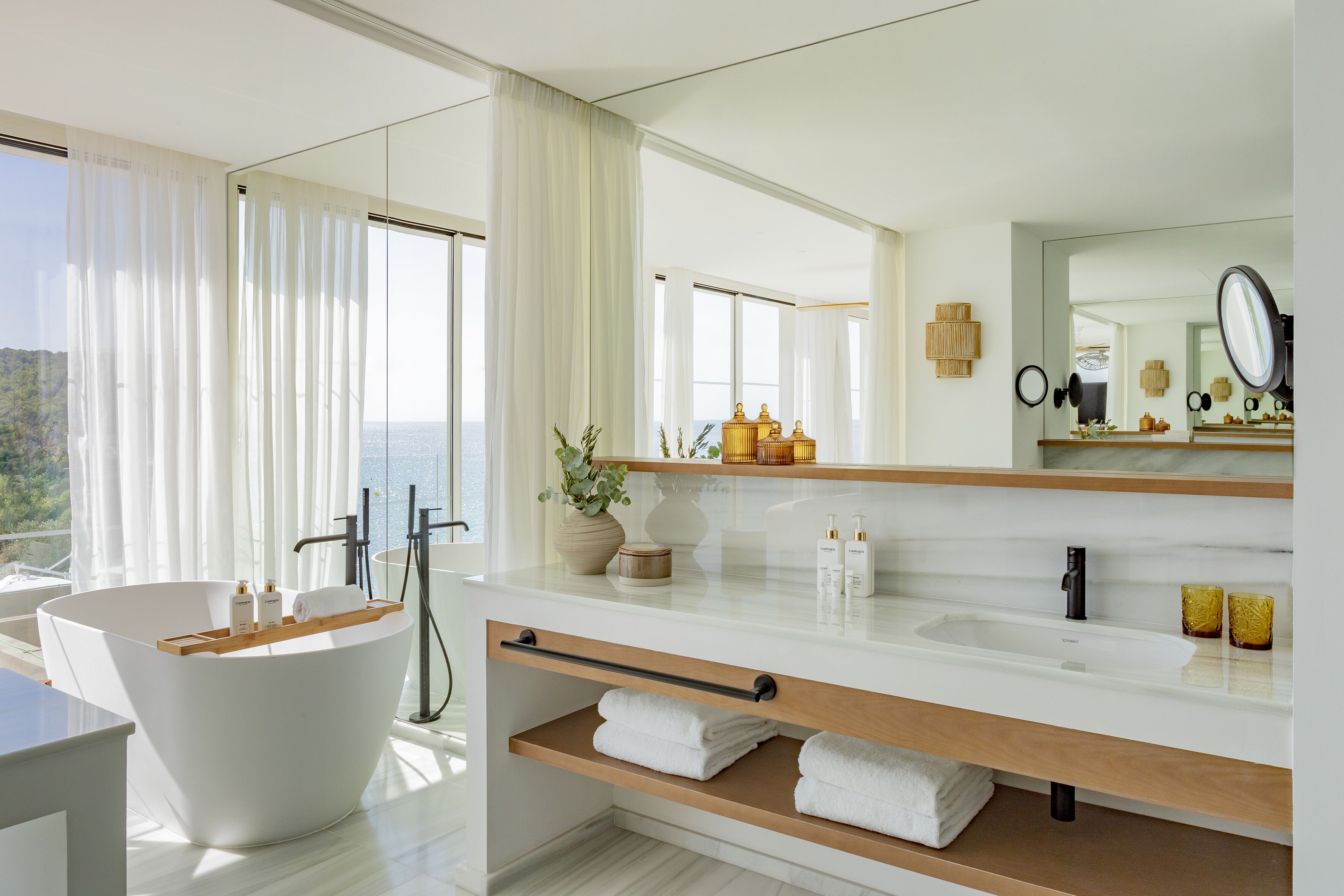 Un baño moderno con una bañera independiente, un espejo grande y vistas al exterior.