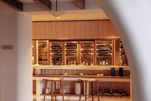 A bar area with wooden shelves displaying bottles, a counter with stools, and a sign reading "SAO".