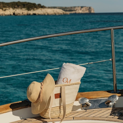 A boat deck with a hat and a towel, a metal railing, and a view of the sea and cliffs.