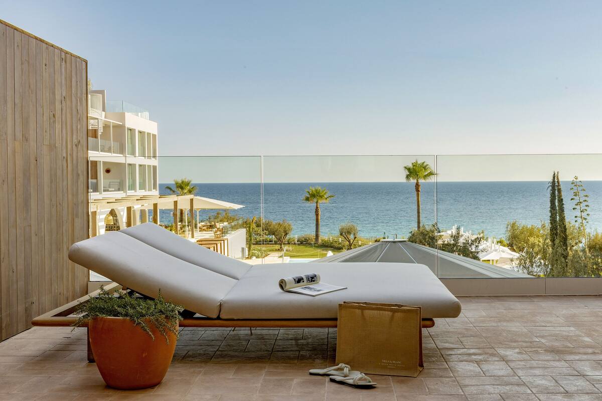 Un fauteuil moderne, avec un magazine, une plante en pot et un sac de courses, est placé sur un balcon donnant sur la mer.