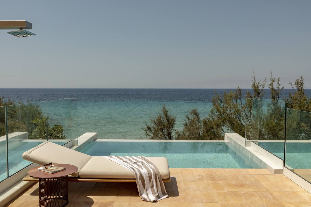 Un espace piscine extérieur moderne offrant une vue dégagée sur la mer, avec un fauteuil de relaxation et une petite table sur laquelle sont posés un livre et des lunettes.