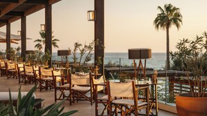 A covered outdoor seating area with wooden chairs and tables, overlooking a body of water.