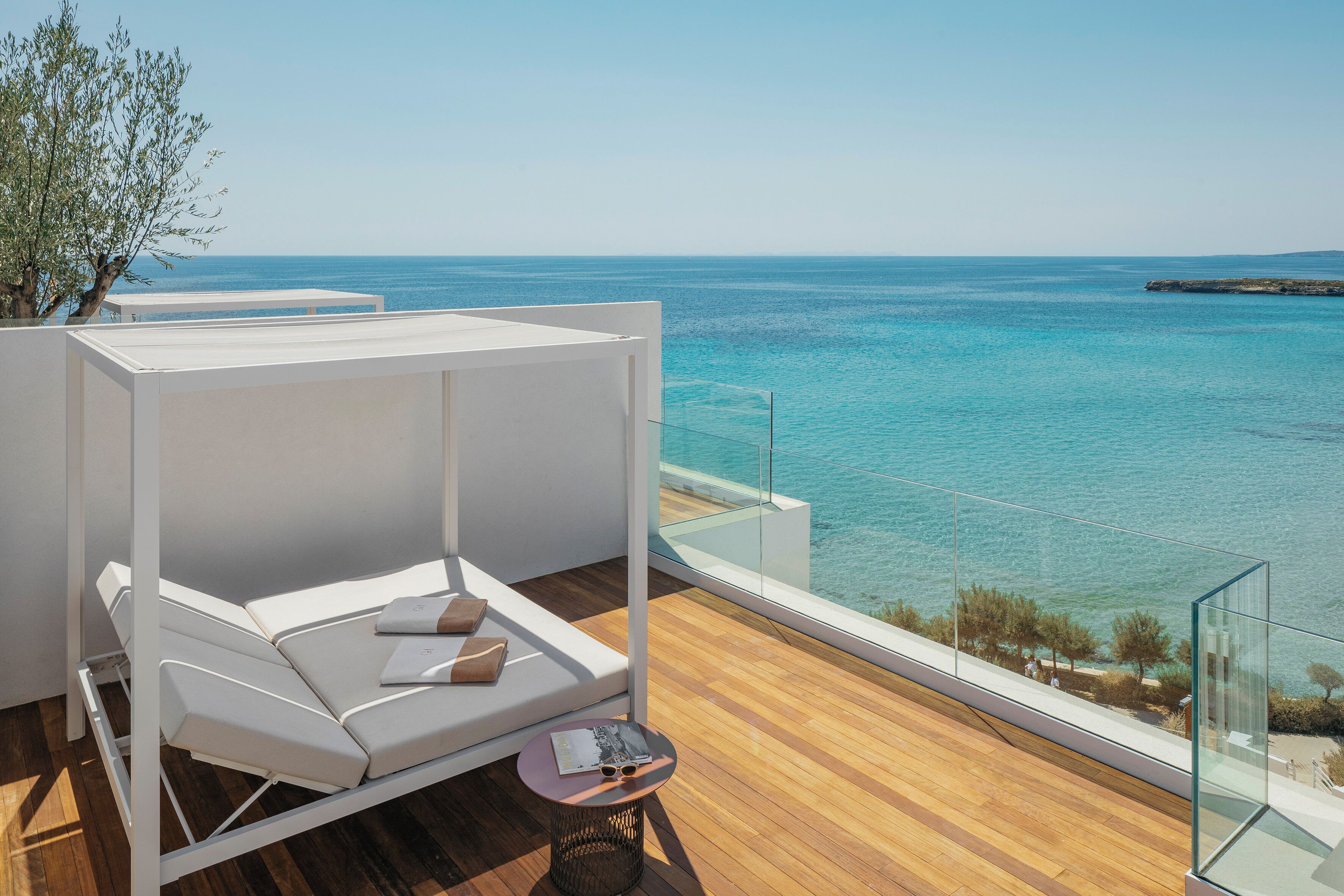 Varanda com sofá branco e mesa pequena, com vista para um mar azul e límpido.