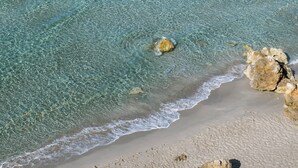 A beach with clear turquoise water, sandy shore, and scattered rocks.