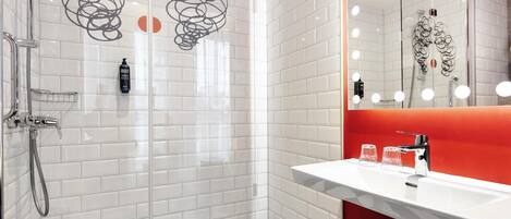 Een moderne badkamer met een glazen douchecabine, een wit wastafelmeubel met een rode accentkleur, en een grote spiegel met verlichting.