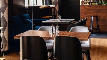 A modern restaurant interior with a wooden table, black chairs, a blue sofa, and a bar area with bottles.