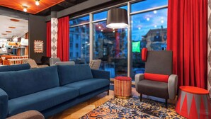 A modern lounge area with a blue sofa, a grey armchair, and a patterned rug. - ibis Styles Szczecin Stare Miasto (Szczecin)