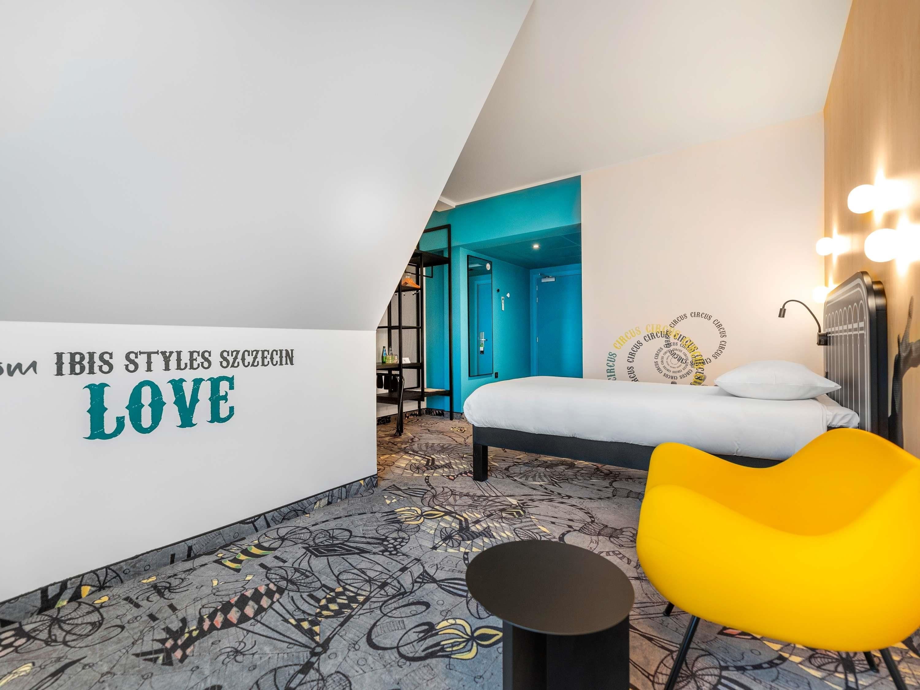 A bedroom with a bed, a yellow chair, a wall with text, and a blue door.