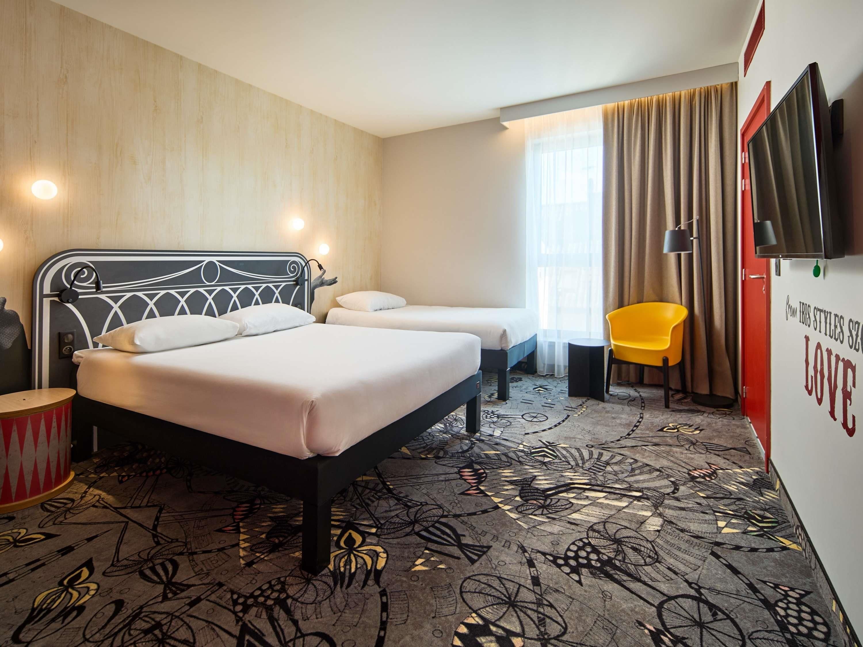 Ein Hotelzimmer mit Bett, Nachttisch, Lampe, Sessel und Fernseher.