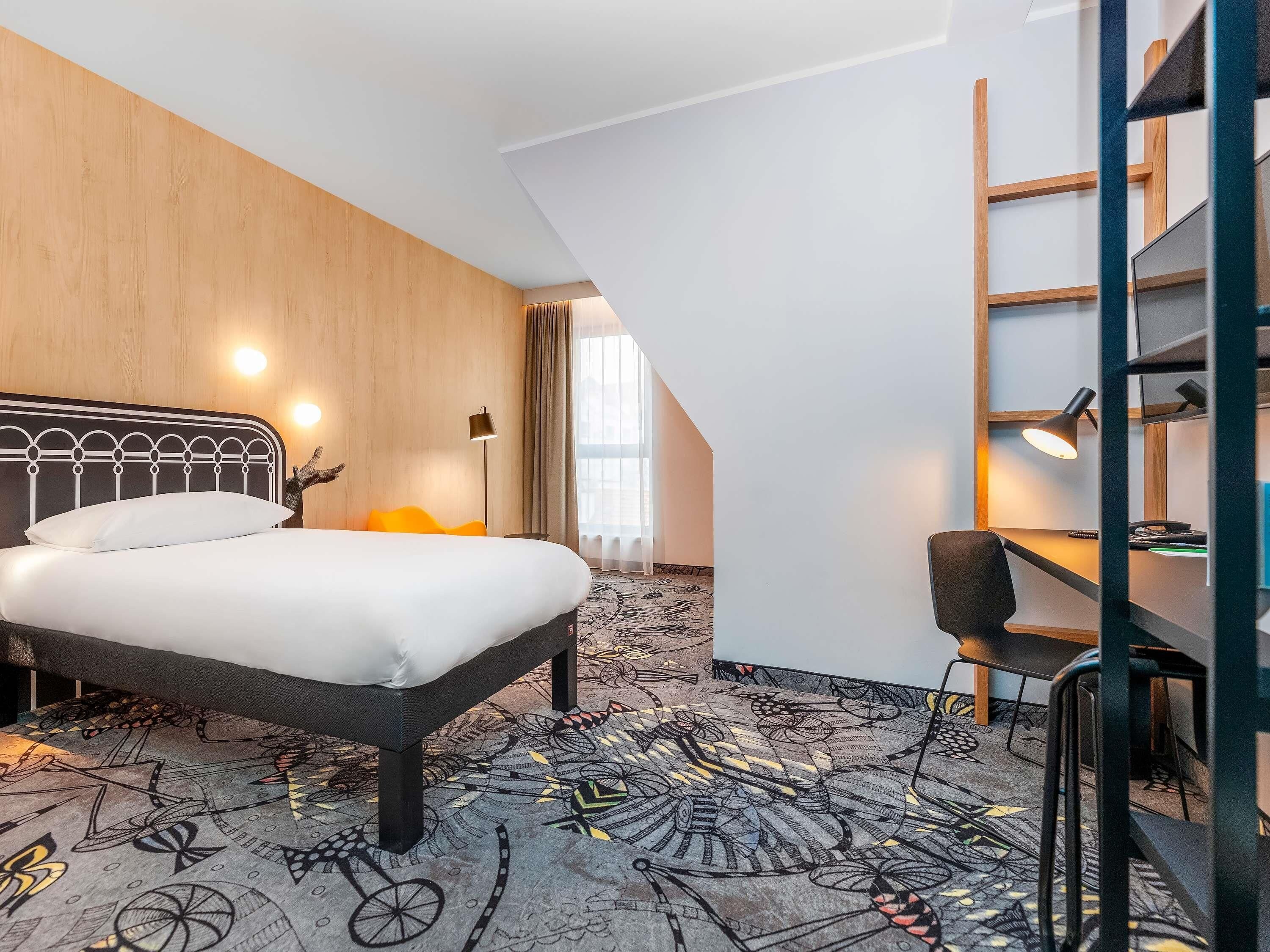 Una habitación de hotel con cama, escritorio, silla y una alfombra de diseño único.
