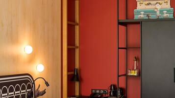 A room with a wooden door, a desk with a lamp, a shelf with suitcases, and a red wall.