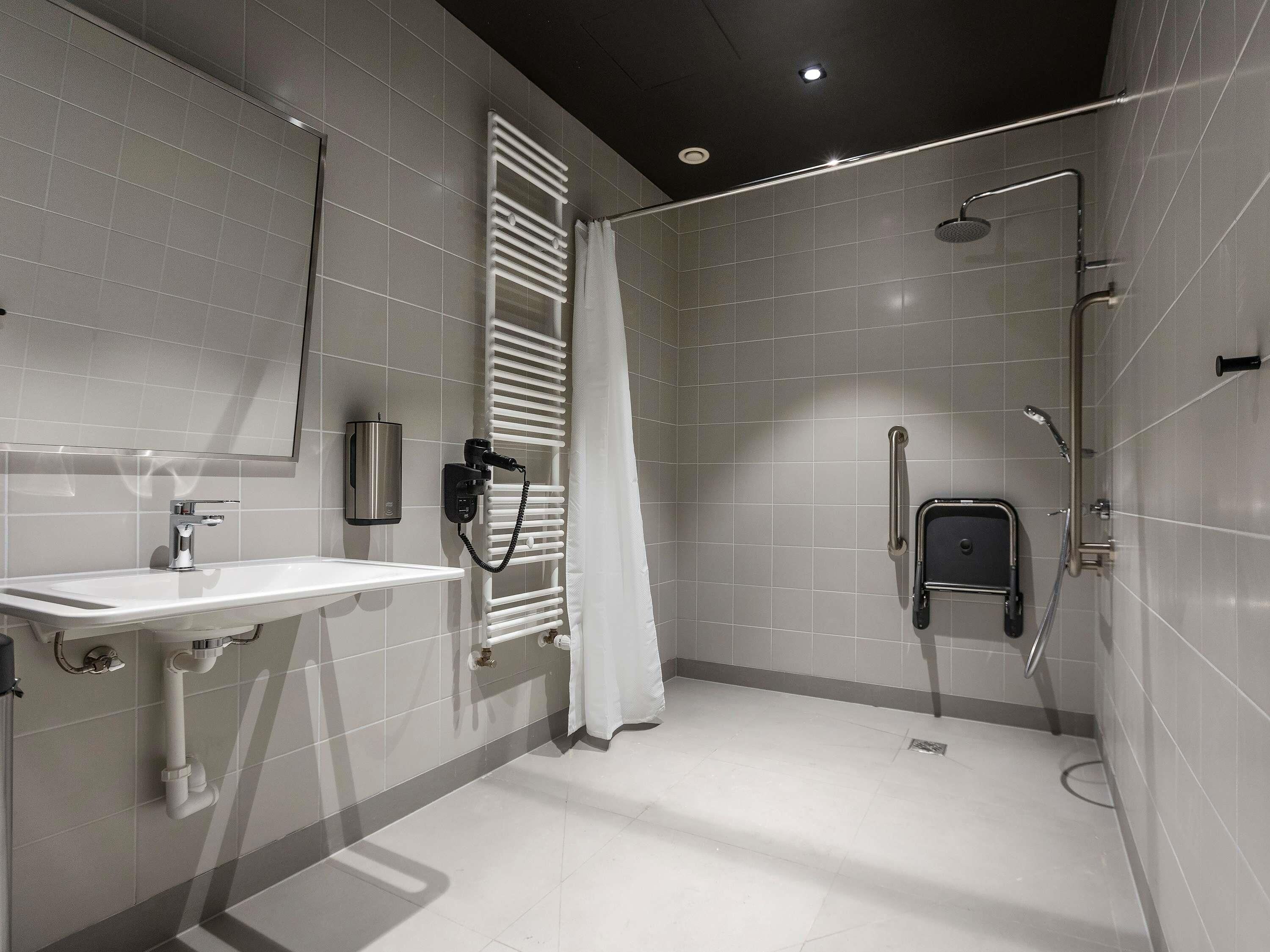 A modern bathroom with a white sink, a heated towel rail, a shower with a handheld showerhead, and a glass-enclosed shower stall.