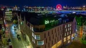 A hotel with a modern design, located in a city with a view of a large Ferris wheel and a bridge in the background. - ibis Styles Szczecin Stare Miasto (Szczecin)