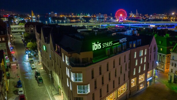 A hotel with a modern design, located in a city with a view of a large Ferris wheel and a bridge in the background. - ibis Styles Szczecin Stare Miasto (Szczecin)