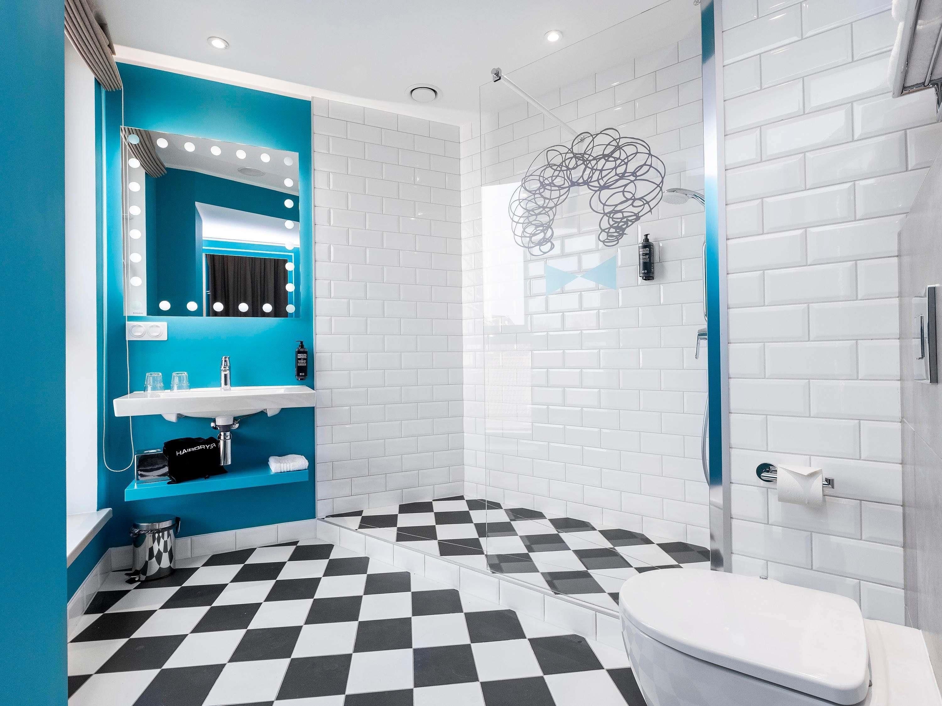 Een badkamer met een blauwe accentmuur, een wit wastafelmeubel, een zwart-wit schakeleffect vloer en een wit toilet.