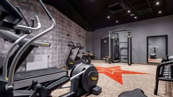 Gimnàs amb màquines cardiovasculars, zona de musculació i mirall que reflecteix material esportiu.