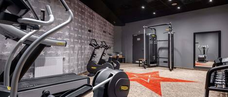 A gym with cardio machines, a weightlifting area, and a mirror reflecting exercise equipment.