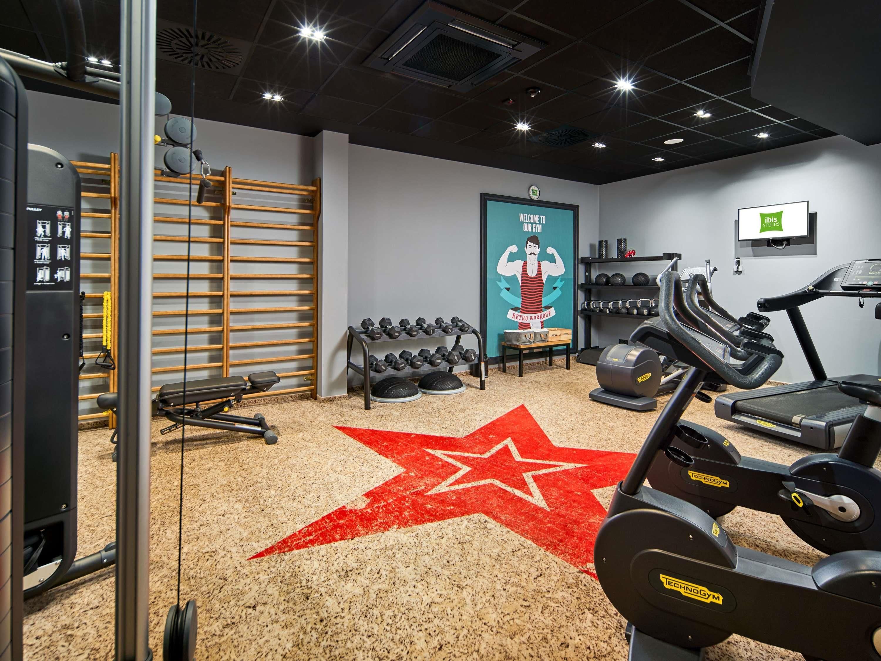 Une salle de sport équipée de matériel d’exercice, un tapis orné de motifs en forme d’étoiles et un panneau d’accueil.