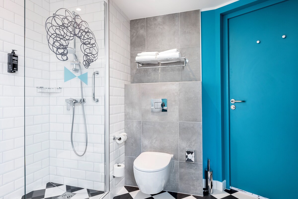 A modern bathroom with a glass shower enclosure, a white toilet, and a blue door.
