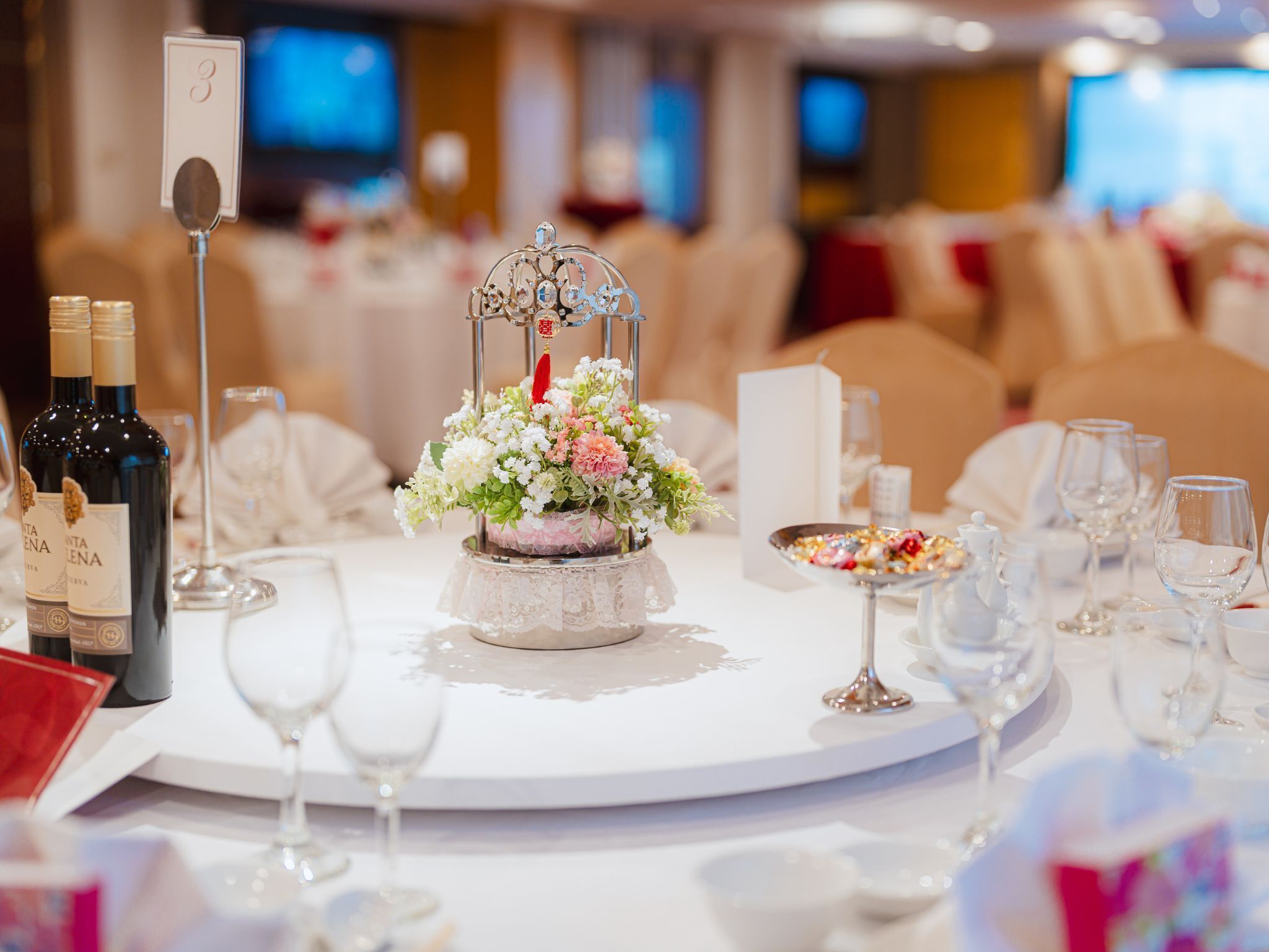 A round table with a floral centerpiece, wine bottles, and glasses.