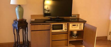 A compact kitchenette with a microwave, coffee maker, and a flat-screen TV on a wooden counter.