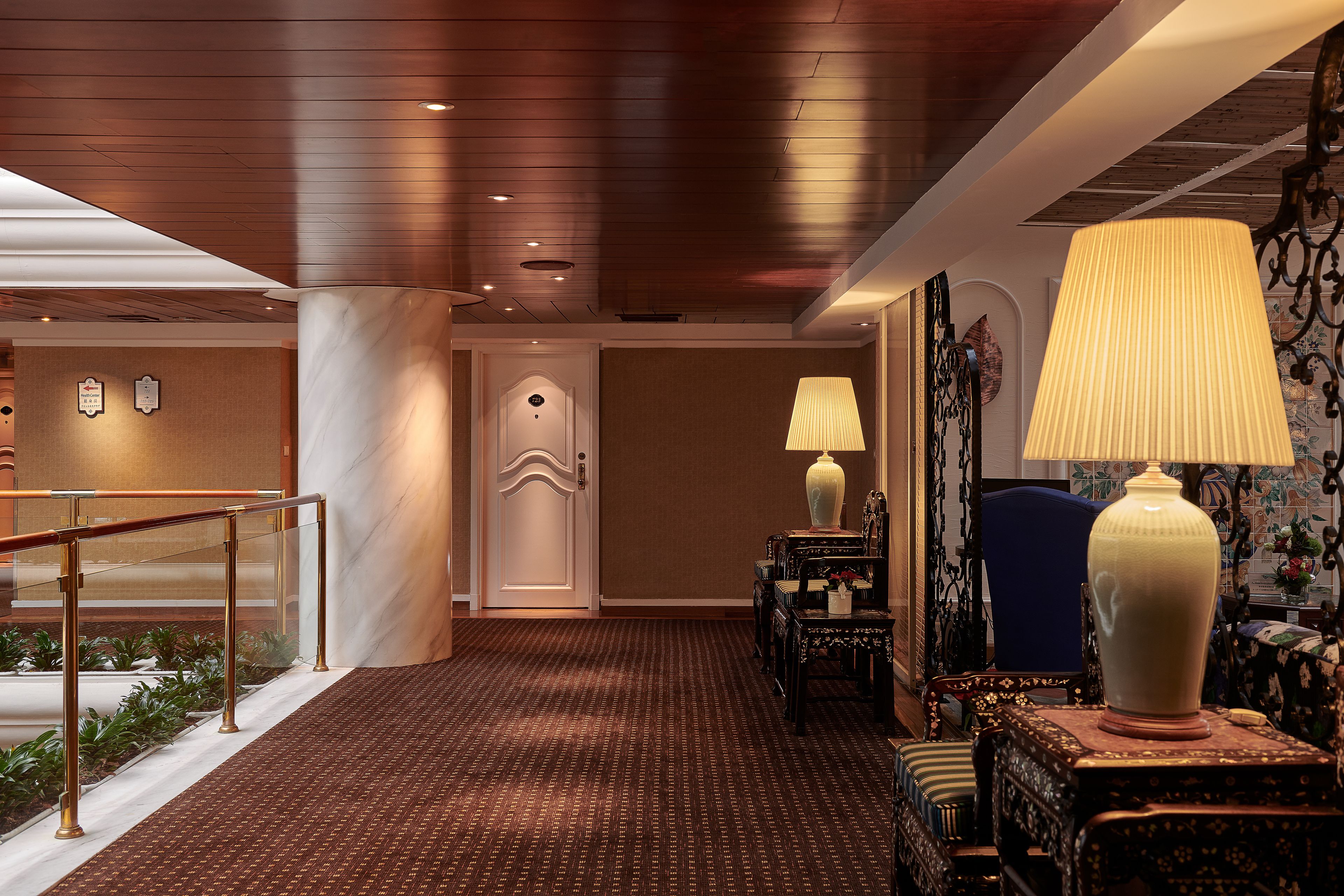 A hotel lobby with a marble column, a patterned carpet, a reception desk, and a blue chair.