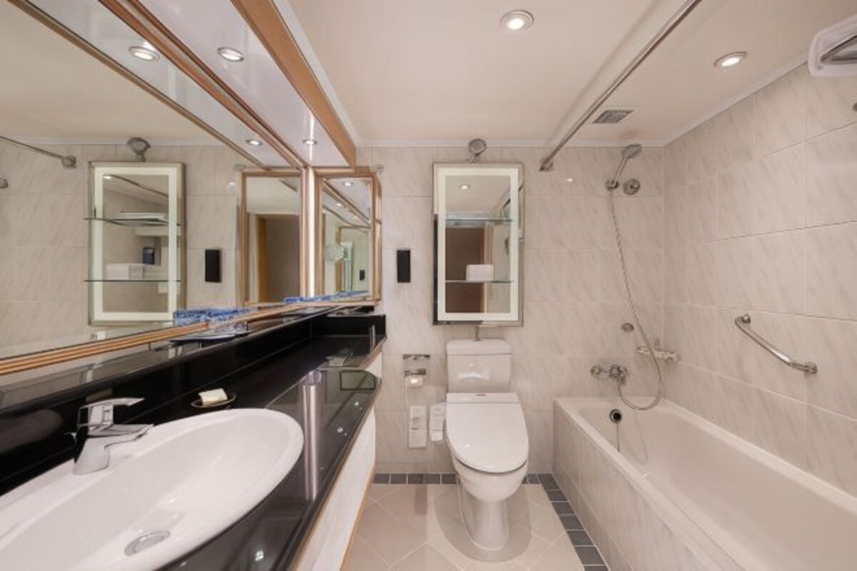 A modern bathroom with a large mirror, a sink, a toilet, and a bathtub.