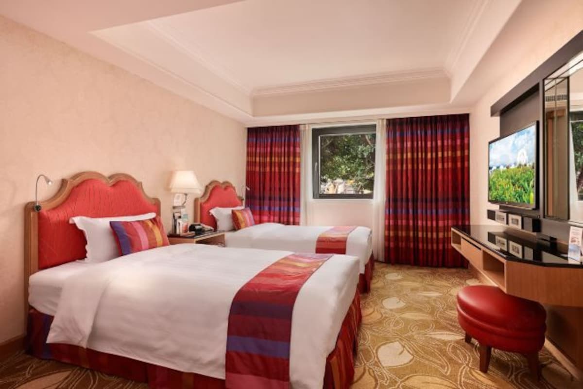 A hotel room with two beds, a desk with a television, and a window with curtains.