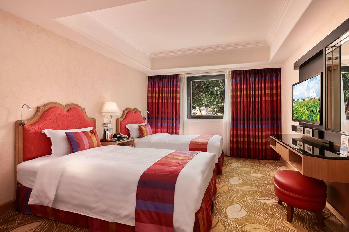 Hotellihuone, jossa on kaksi sänkyä, televisio, työpöytä ja ikkuna, jossa on verhot.