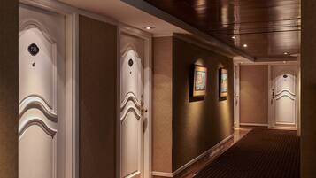 A hotel hallway with three doors, each with a number plate. The walls are textured, and there are framed pictures on the wall.