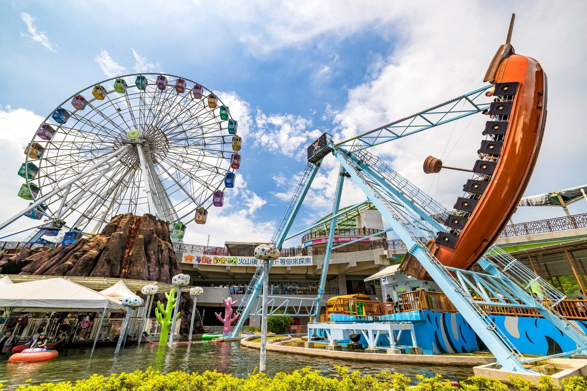 A water ride with a Ferris wheel and a roller coaster in the background.