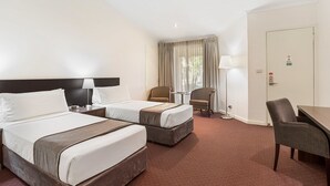 Une chambre d’hôtel avec deux lits, un bureau, une chaise, une lampe et une fenêtre avec des rideaux.