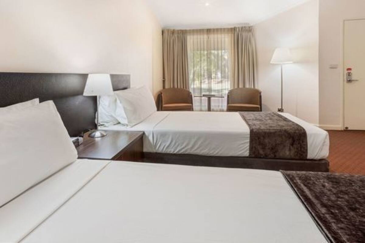 A hotel room with two beds, a nightstand, a lamp, a chair, and a window with curtains.